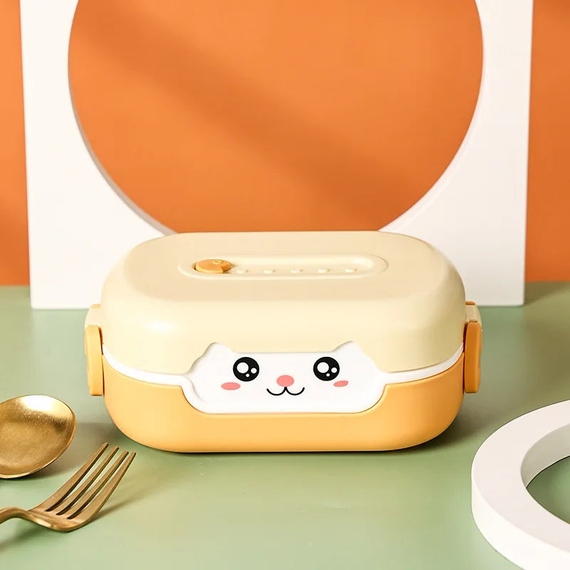 Cute cartoon-style kawaii lunch box with a face on a green surface with a gold spoon and white plate.
