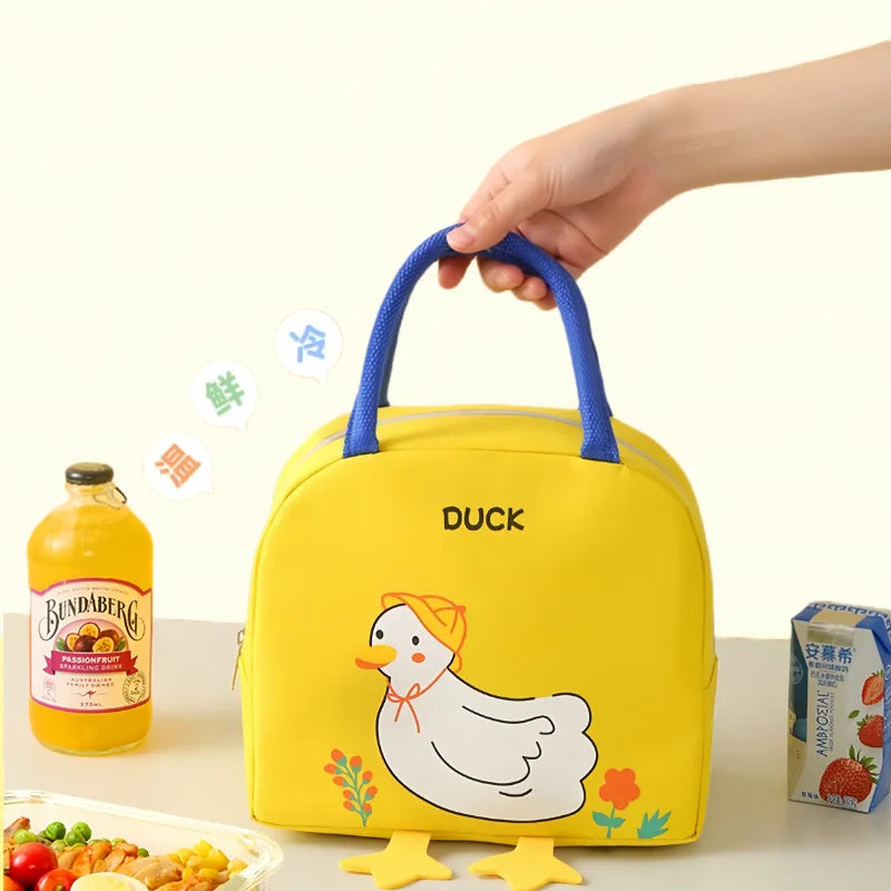 Yellow kawaii lunch bag with duck design held by a hand, surrounded by snacks and juice on a white background.