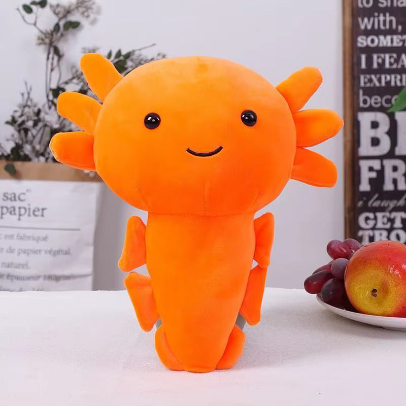 Orange plush axolotl toy on a white surface with grapes and an apple in the background.