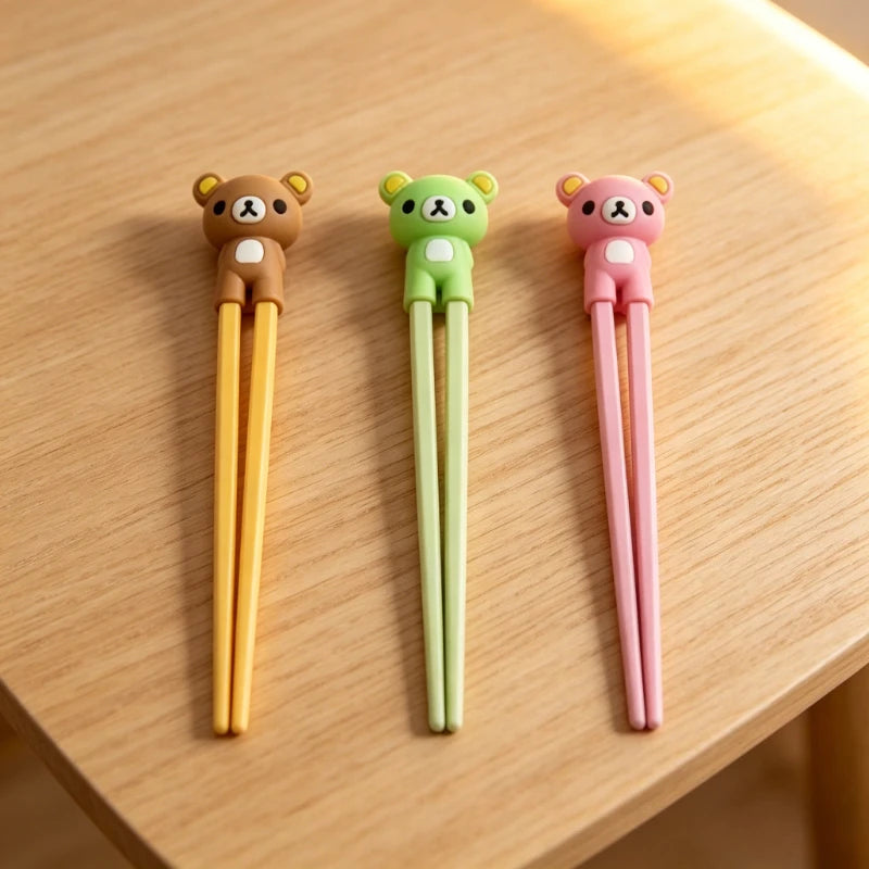 Three cartoon bear-shaped kawaii chopsticks in yellow, green, and pink on a wooden surface.