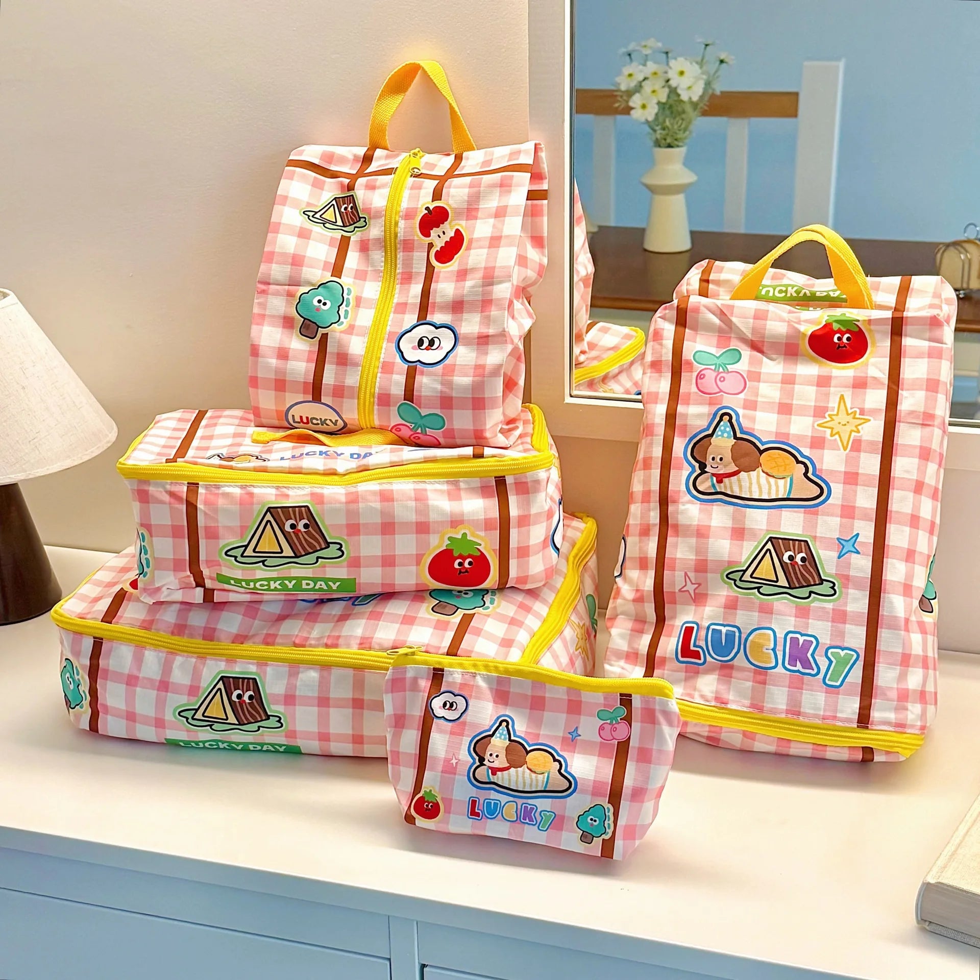 Set of pink checkered luggage bags with Kawaii cartoon designs on a table.