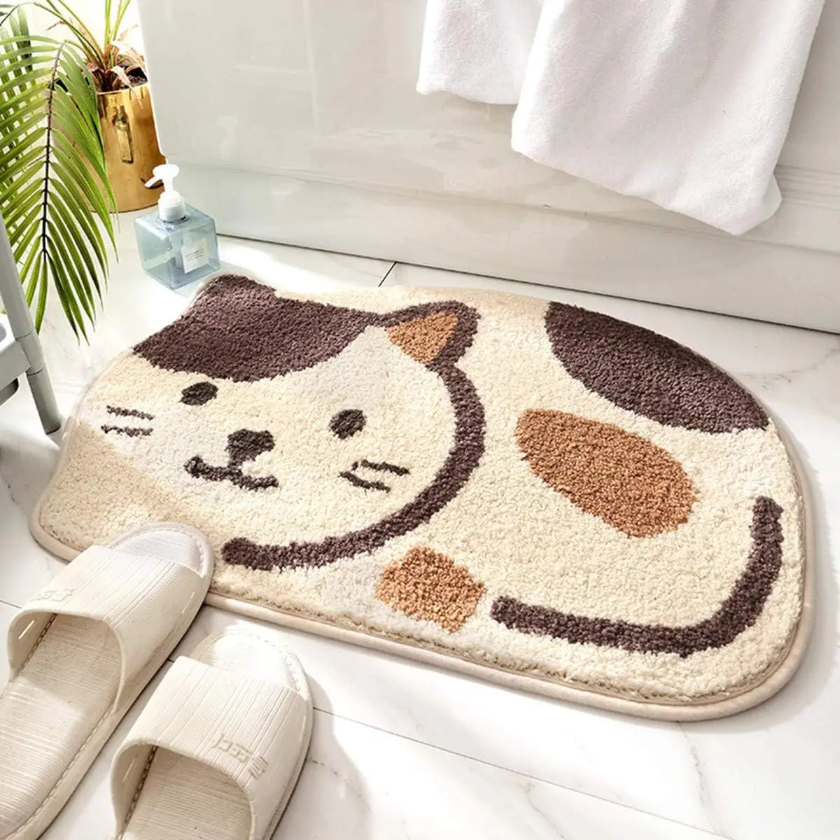 Cat-shaped kawaii bath mat on a bathroom floor with slippers and towels in the background.