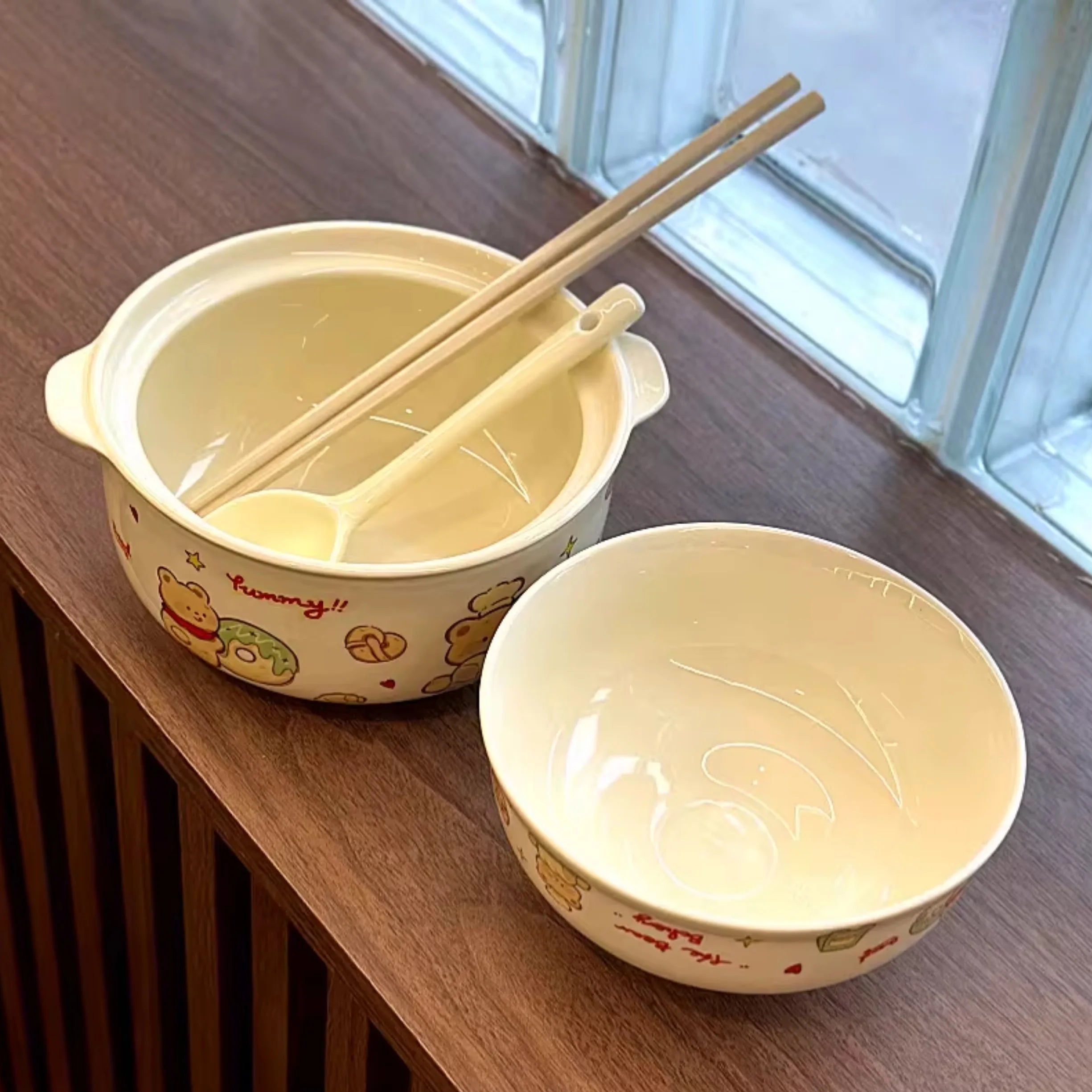 Two ceramic kawaii ramen bowls with cartoon designs on a wooden surface.