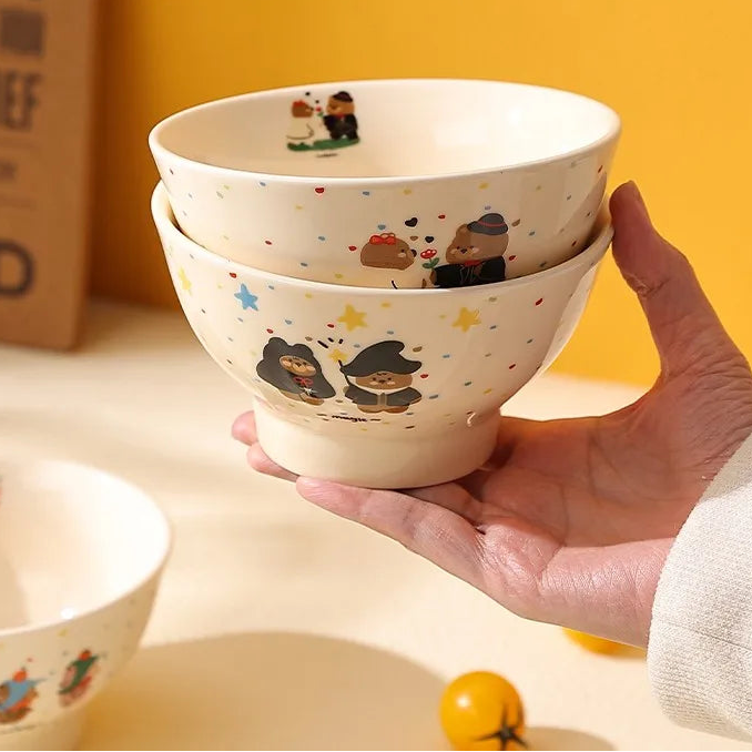 Hand holding a stack of ceramic kawaii ramen bowls with cartoon designs on a yellow background