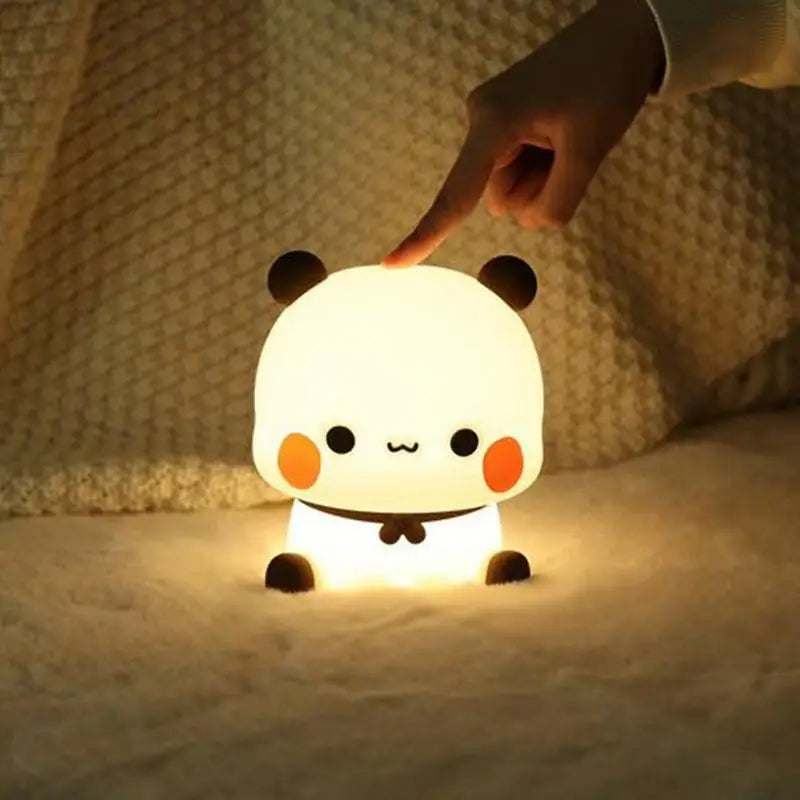 Cute panda-shaped kawaii night light being touched by a hand on a soft surface.