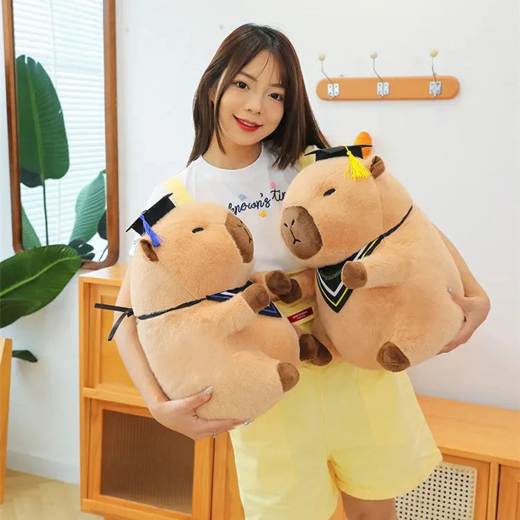 Woman holding two large kawaii plush toys resembling animals with graduation caps indoors.