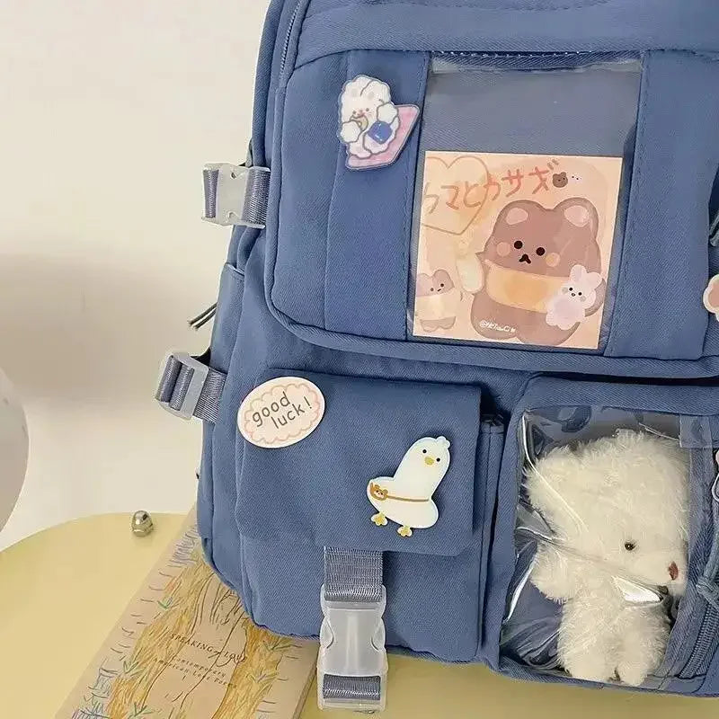 Blue backpack with various items including a Kawaii plush toy, stickers, and a card on a light background.