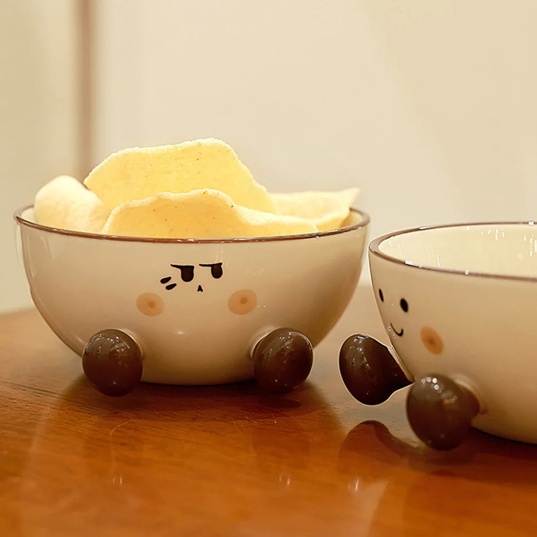 Two ceramic kawaii ramen bowls with cartoon faces on a wooden surface