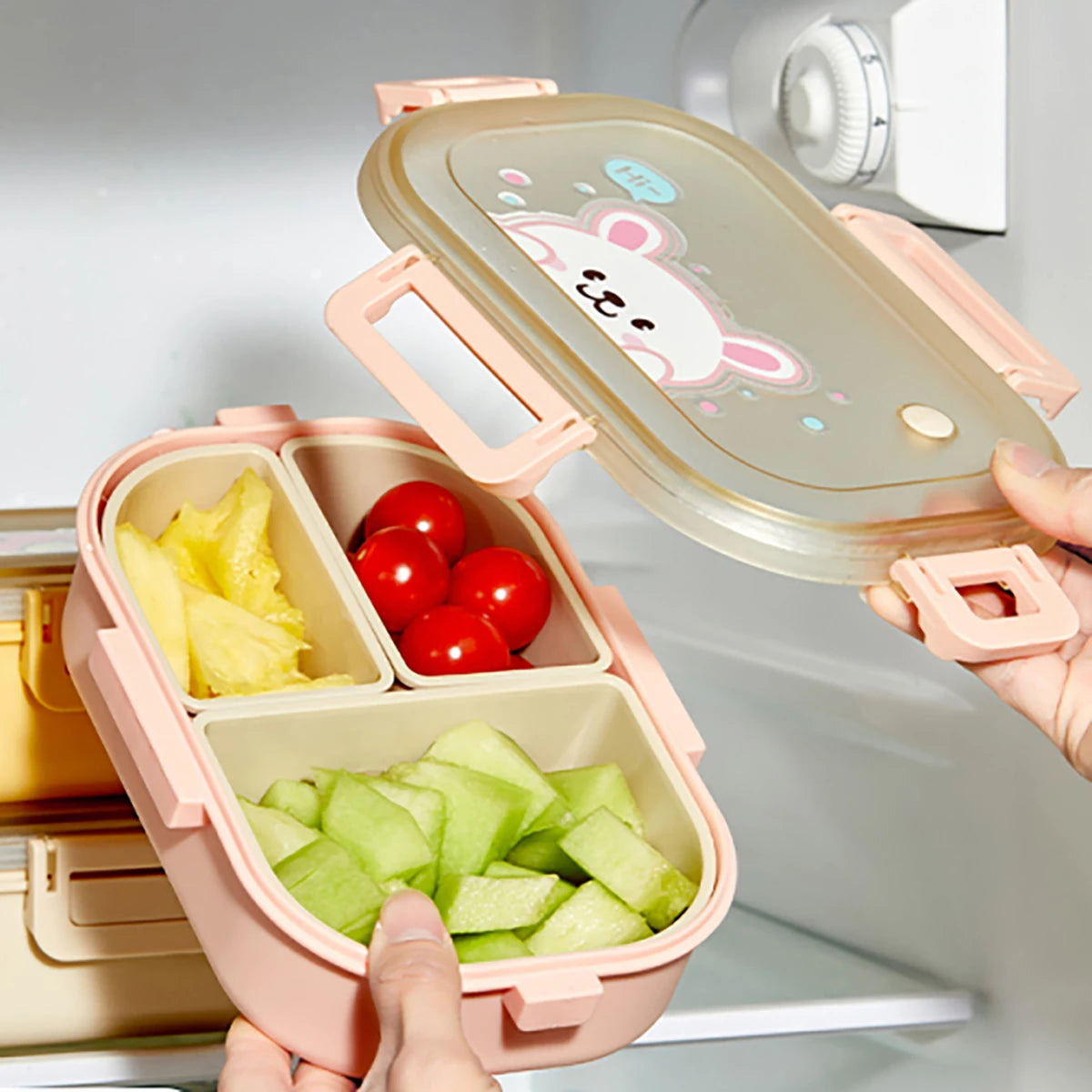 Pink kawaii bento box with compartments of fruits and vegetables, held in front of a refrigerator.
