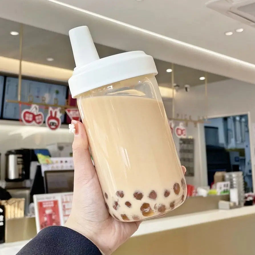Hand holding a clear kawaii cup with a white lid filled with bubble tea in a store setting