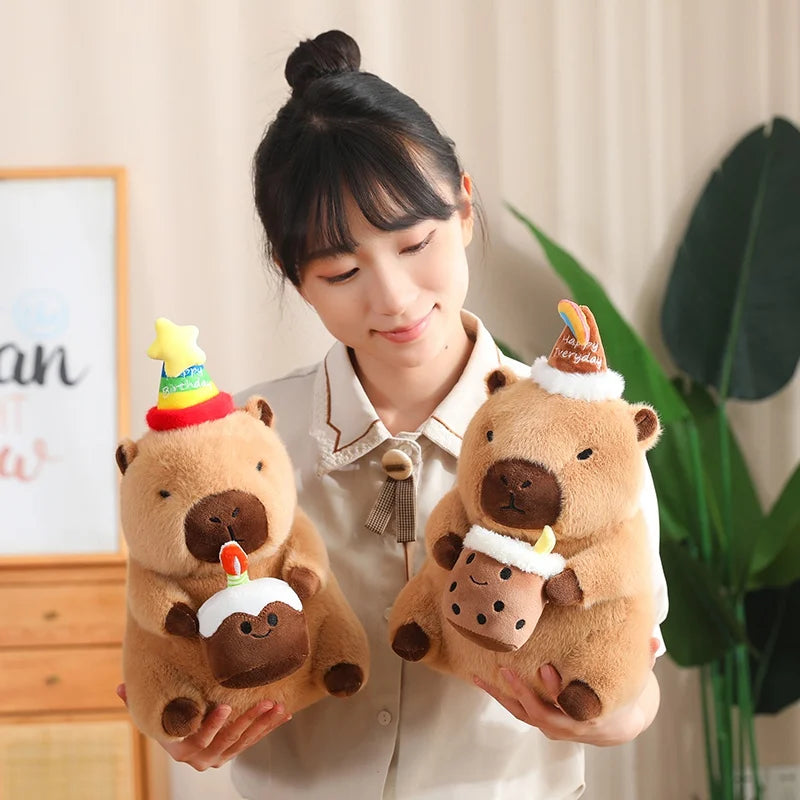 Person holding two capybara plush toys beavers with decorative hats indoors.