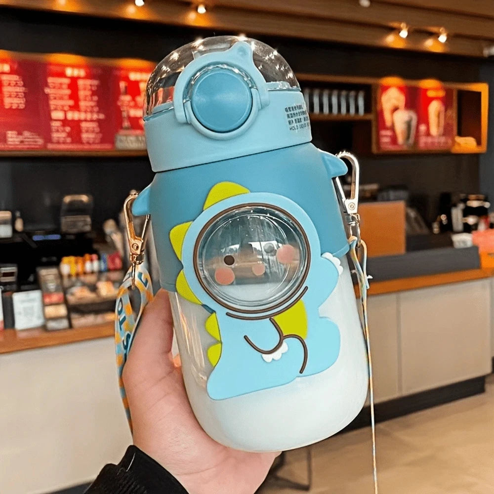 Colorful kawaii water bottle with dinosaur design held in a hand inside a coffee shop.