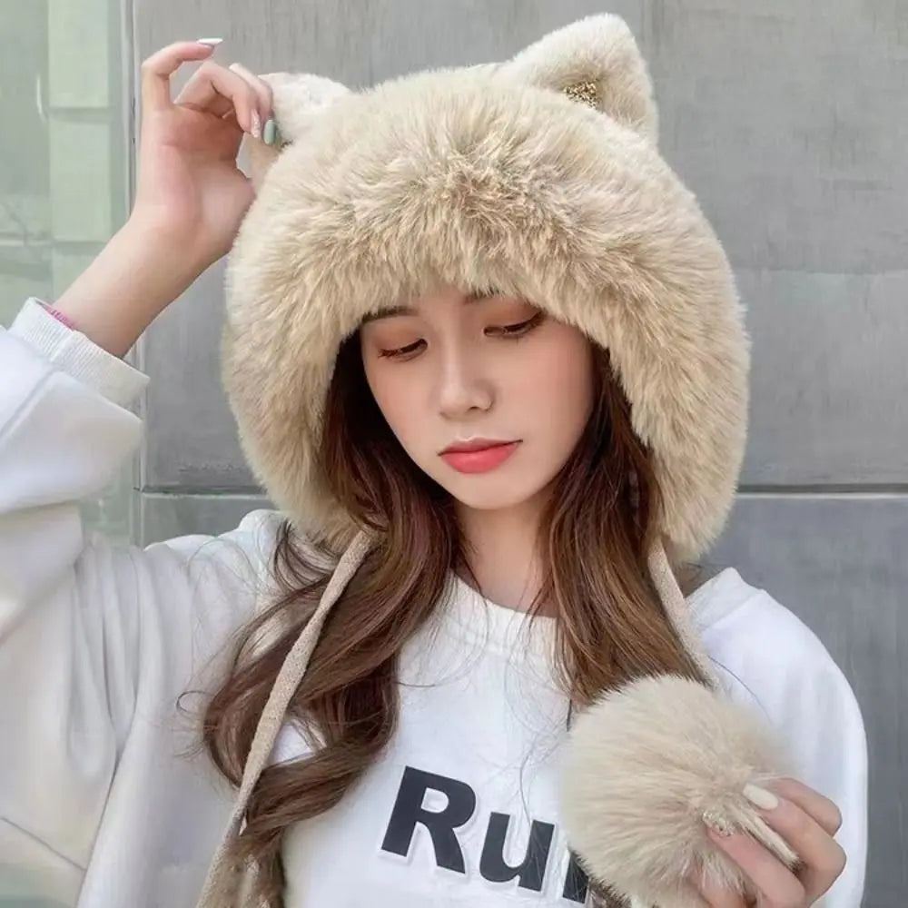 Person wearing a fluffy beige Kawaii hat with cat ears and pom-poms, holding the hat with one hand.
