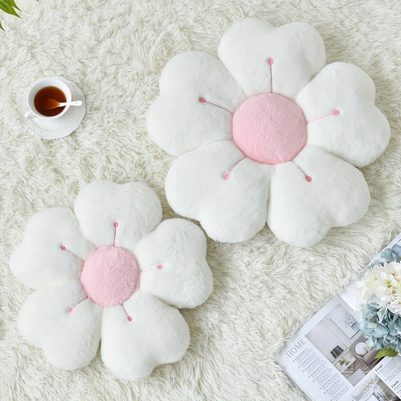 Flower-shaped kawaii cushions on a fluffy white surface with a cup of tea and magazine.