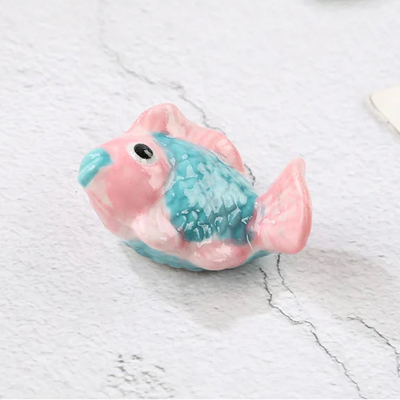 Small pink and blue fish-shaped kawaii chopstick holders on a light gray surface with text overlay.