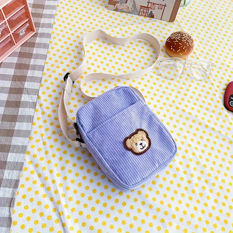 Small blue textured bag with a bear patch on a yellow polka dot tablecloth.