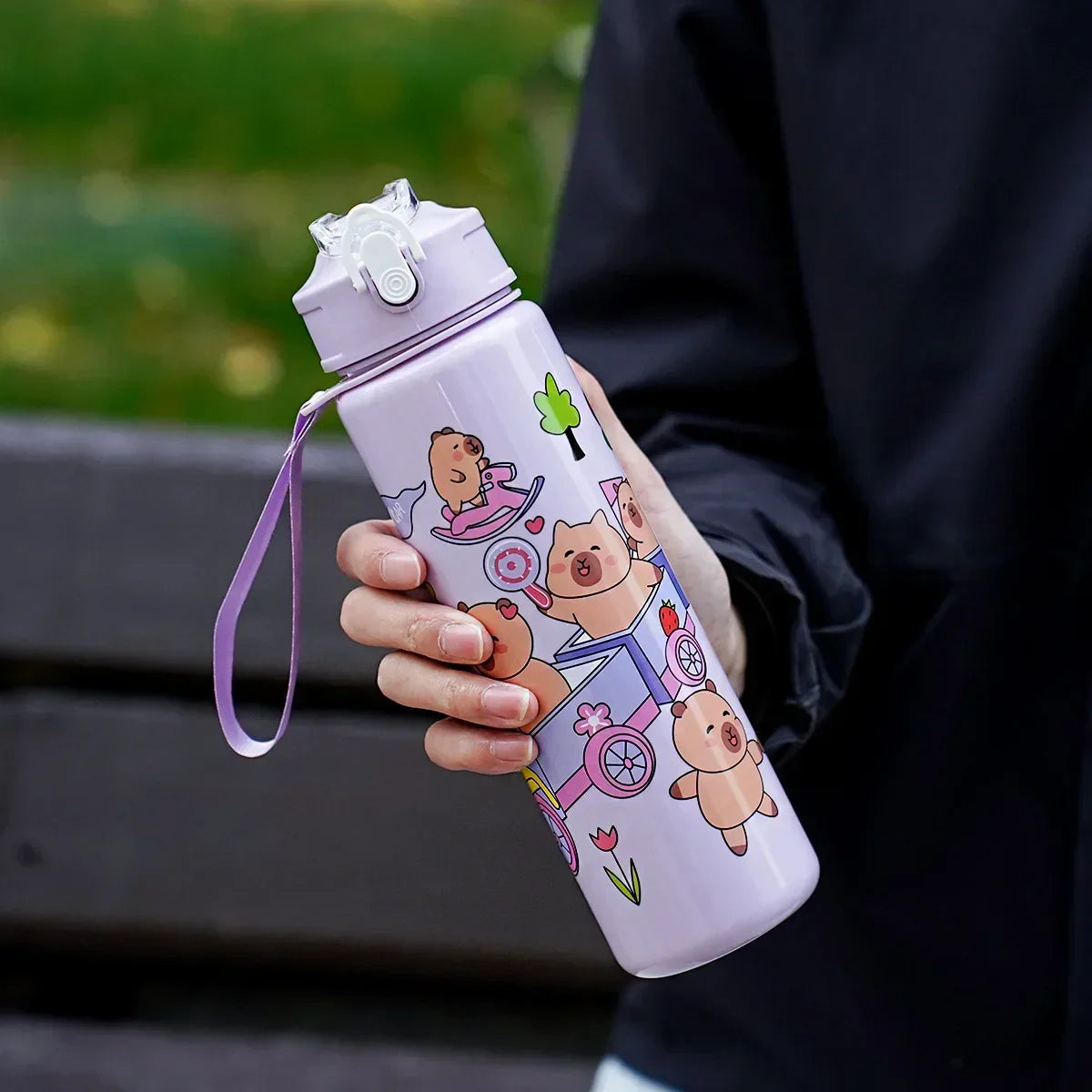 Person holding a pink kawaii water bottle with cartoon designs outdoors