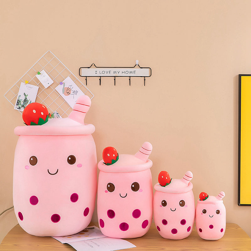 Set of pink kawaii plush drinks with faces on a wooden surface against a beige wall.