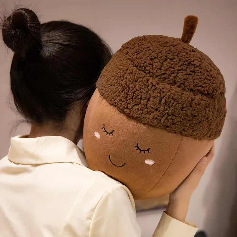 Person wearing a kawaii plush acorn-shaped pillow with a face on a plain background