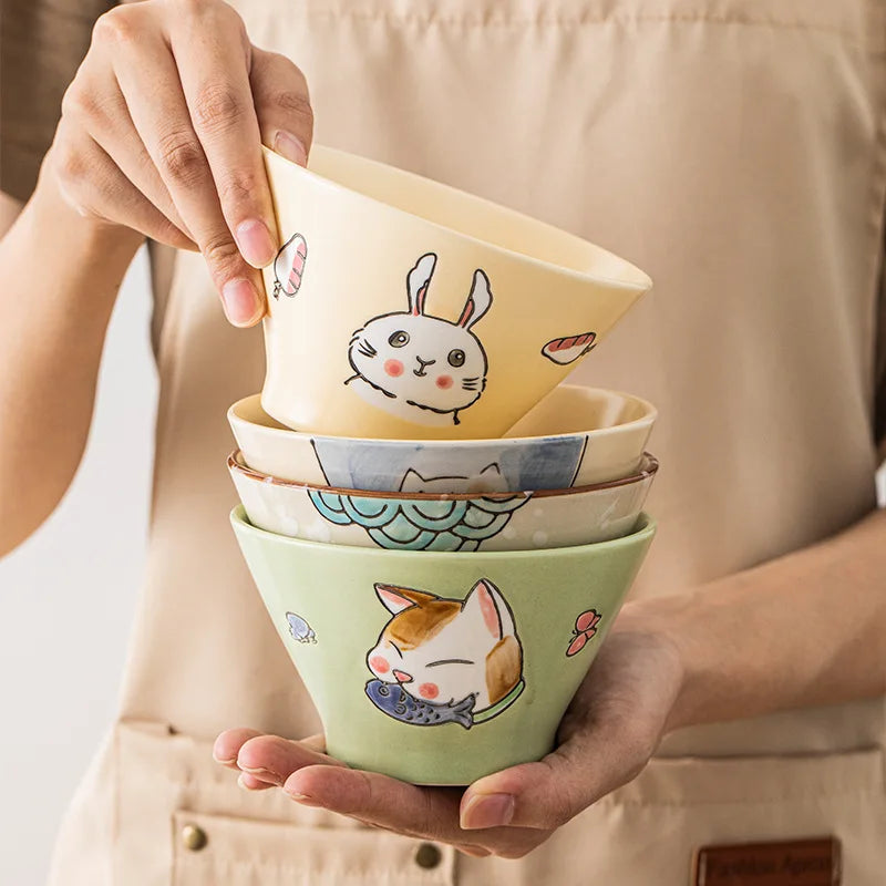 Stack of colorful ceramic kawaii ramen bowls with animal illustrations held by a person.