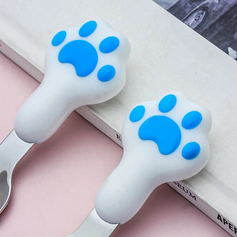 Two white and blue paw-shaped kawaii utensils on a pink surface with books in the background