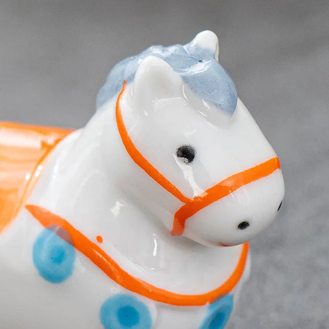White ceramic horse kawaii chopstick holders with orange reins and blue accents on a gray background