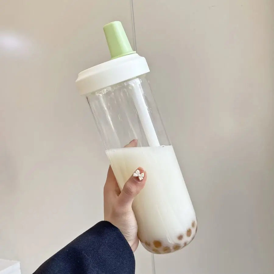Hand holding a clear kawaii water bottle with a green cap filled with a creamy beverage.