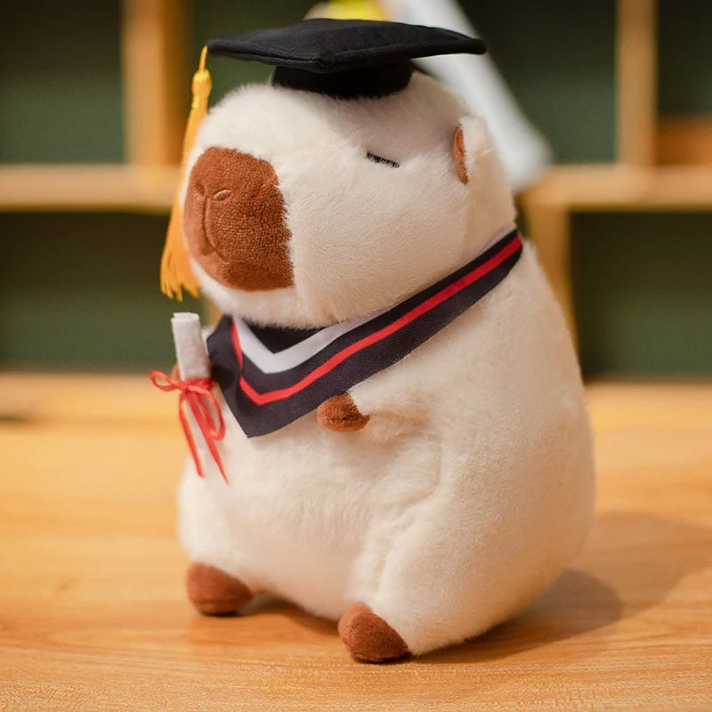 Capybara plush toy wearing a graduation cap and gown on a wooden surface