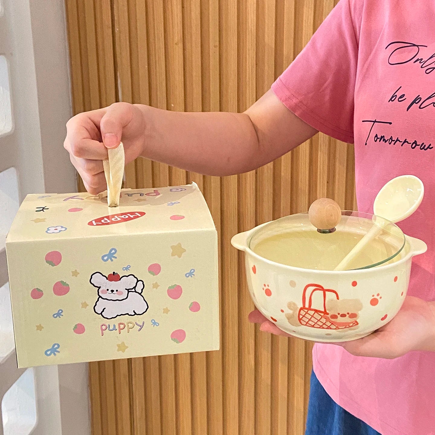 Person holding a cute ceramic kawaii ramen bowl with lid and spoon, next to a matching box with cartoon dog design.