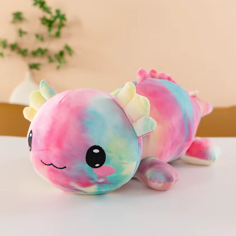 A pastel tie-dye plush toy dragon lying on a white surface with a soft beige background and a blurred plant in the distance.
