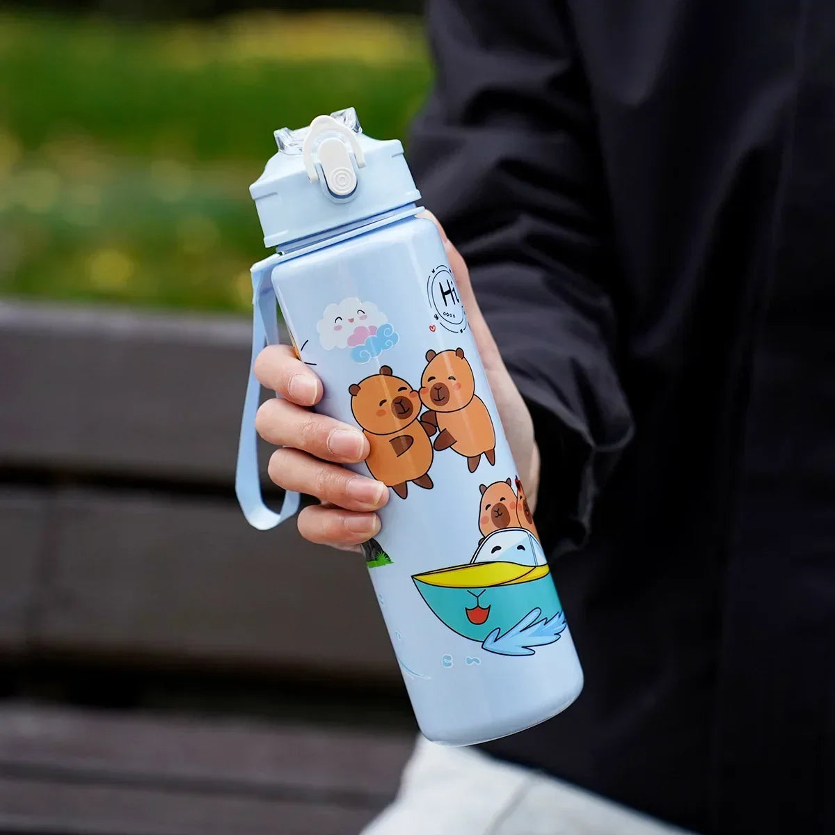 Person holding a light blue kawaii water bottle with cartoon designs outdoors