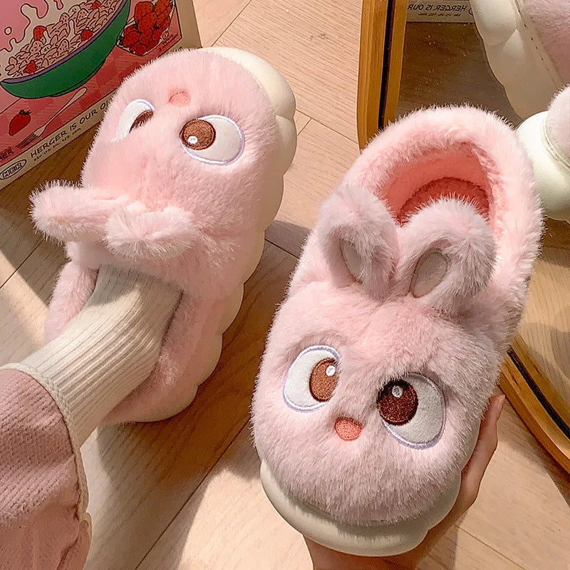 Pair of pink plush kawaii slippers with cartoon face design on a wooden floor.