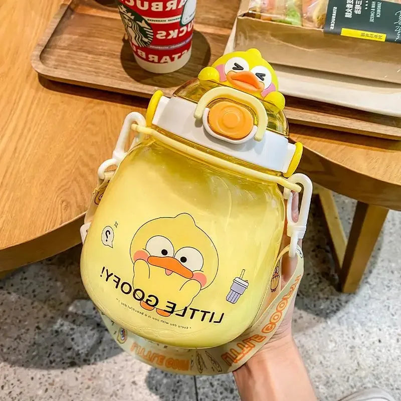 Yellow cartoon duck kawaii water bottle held by a hand on a wooden table with a Starbucks cup in the background.