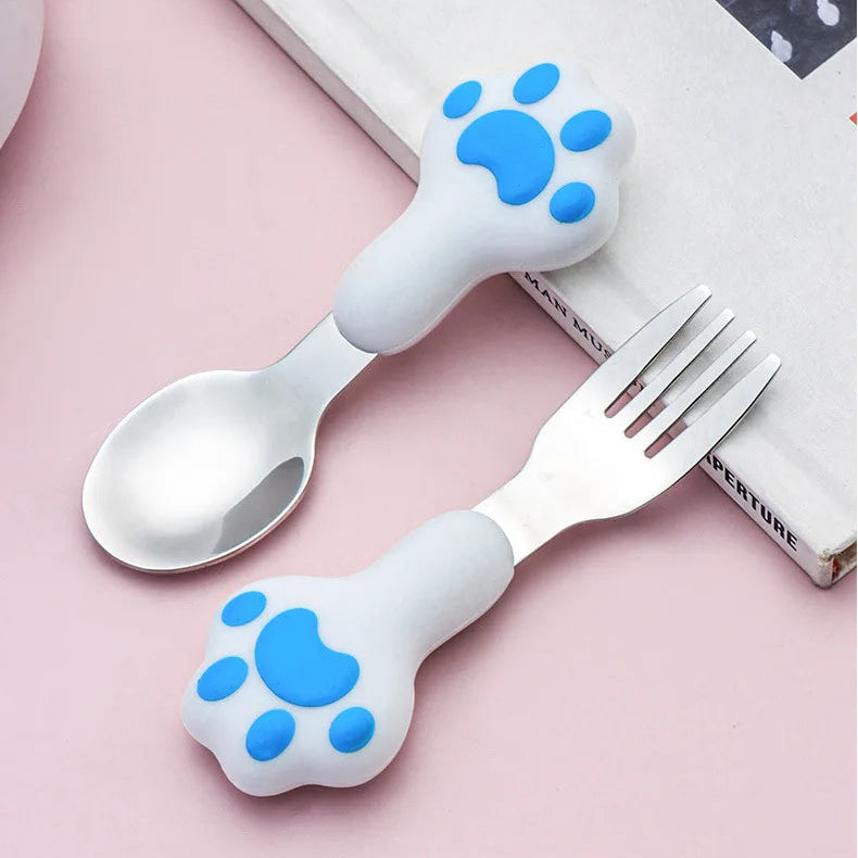 Children's kawaii utensils set with paw-shaped handles on a pink surface.
