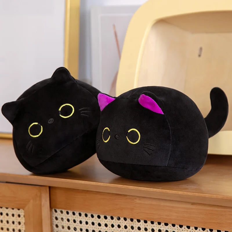 Two black cat-shaped kawaii cushions with pink ears on a wooden surface.