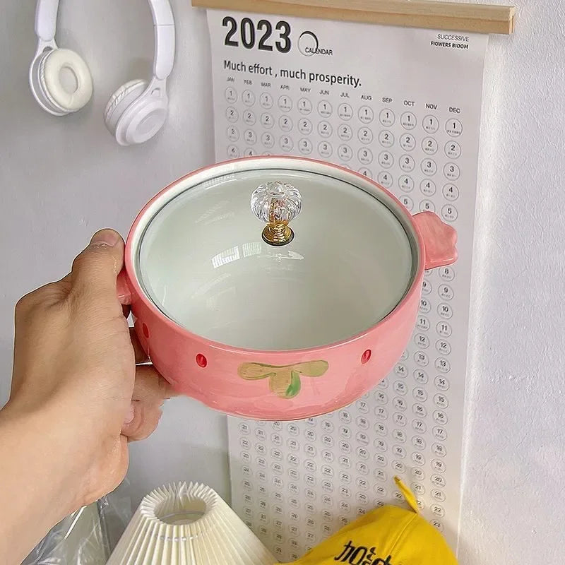 Pink ceramic kawaii bowls with a light bulb inside held by a hand, against a wall with a calendar and headphones.