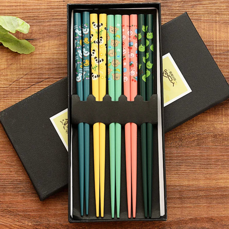 Set of colorful cartoon-themed kawaii chopsticks in a black box on a wooden surface