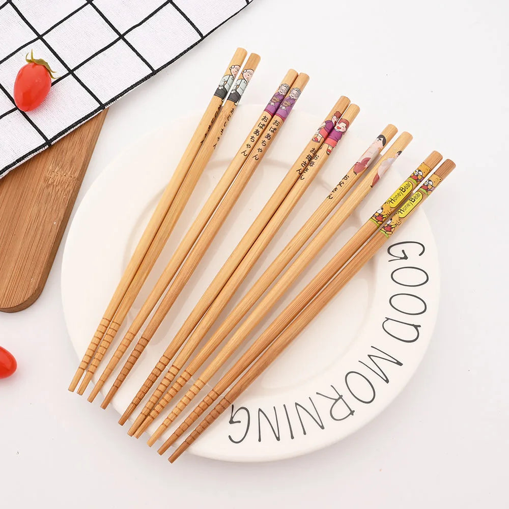 Set of wooden kawaii chopsticks on a white plate with 'Good Morning' text, surrounded by kitchen utensils.