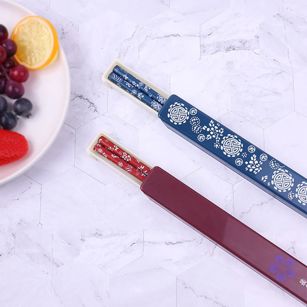 Two decorative kawaii chopsticks with intricate patterns on a marble surface with fruits in the background.