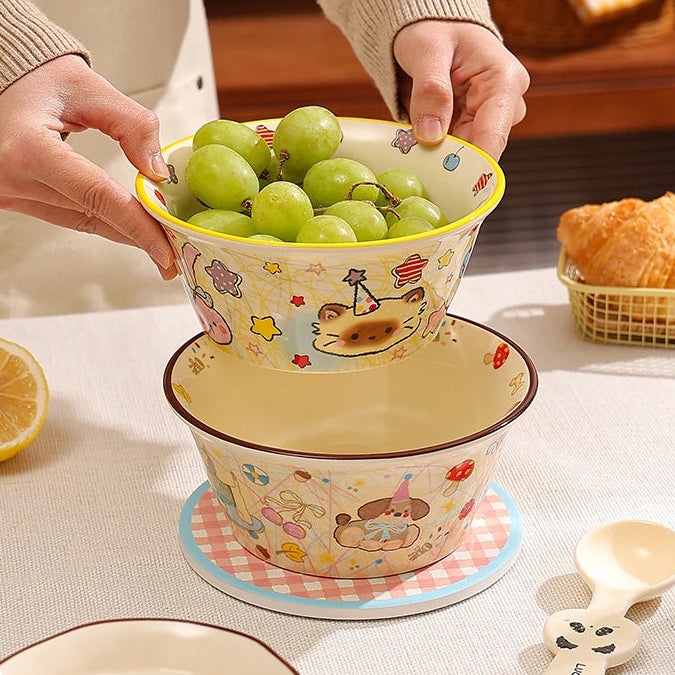 Person holding a kawaii ramen bowl of grapes with a set of cartoon-themed ceramic dishes on a table.