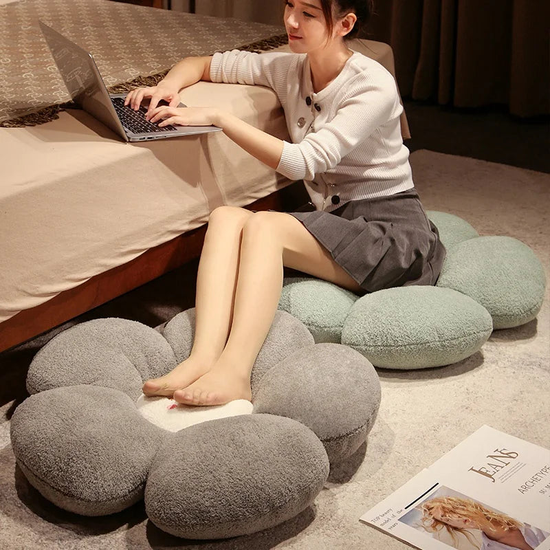 Woman sitting on a cloud-shaped kawaii pillow using a laptop in a cozy room.