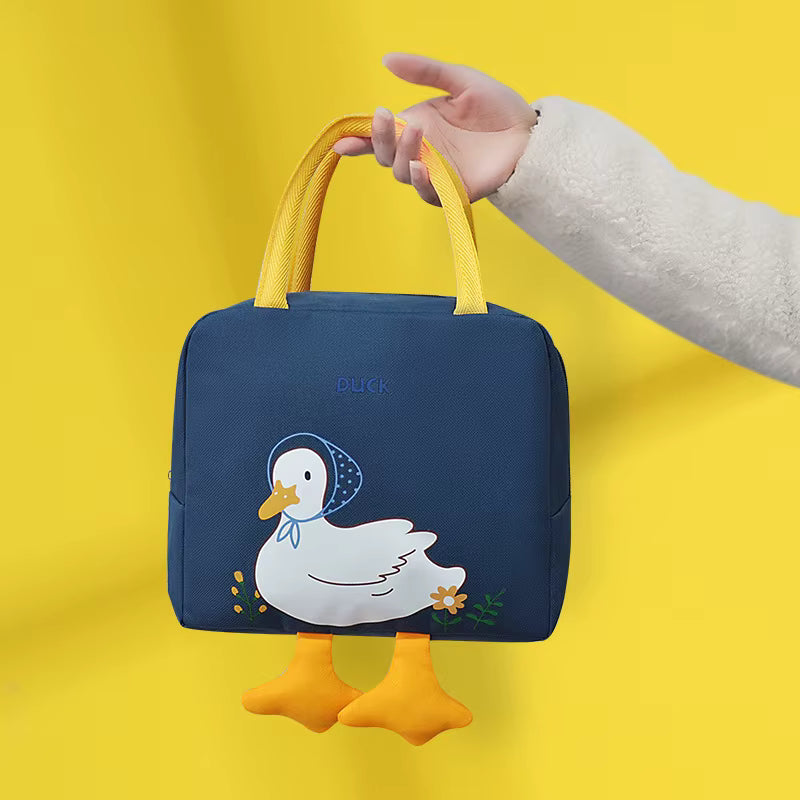 A navy blue insulated lunch bag with yellow handles, featuring a cartoon duck design on the front and two dangling yellow duck feet charms. A hand in a white sleeve holds the bag against a solid yellow background.