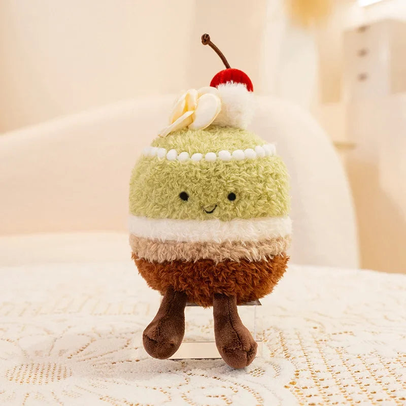 Kawaii plush toy resembling a layered dessert with a cherry on top, sitting on a textured surface.