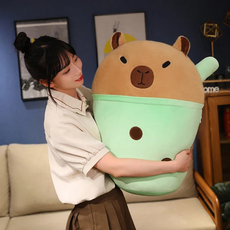 Person holding a large, plush, bear-shaped kawaii pillow with a blue wall and framed pictures in the background.