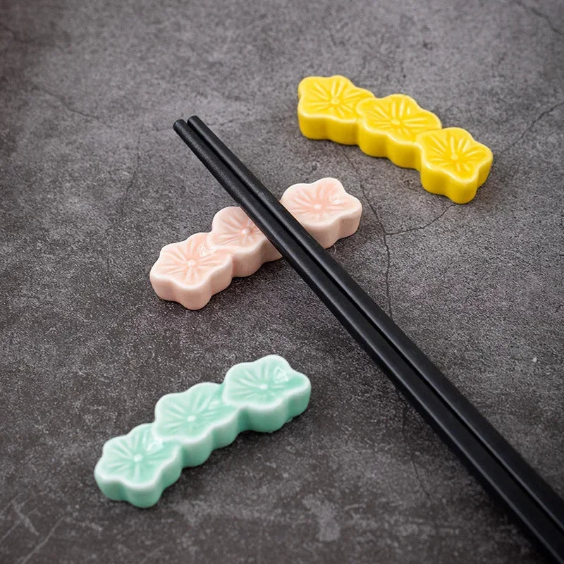 Three colorful ceramic kawaii chopstick holders on a gray surface with black chopsticks.