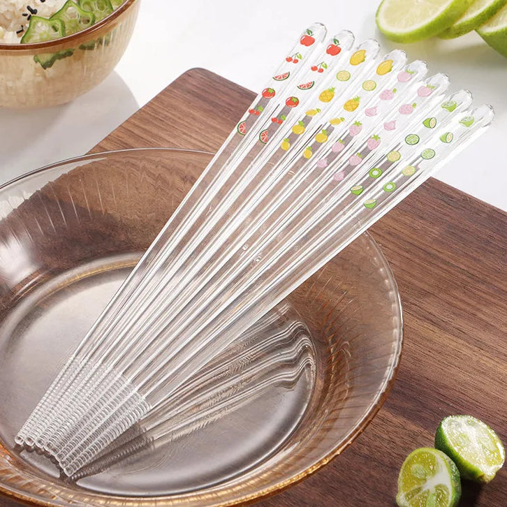 Set of clear kawaii chopsticks with colorful designs on a wooden surface with limes and a bowl in the background.