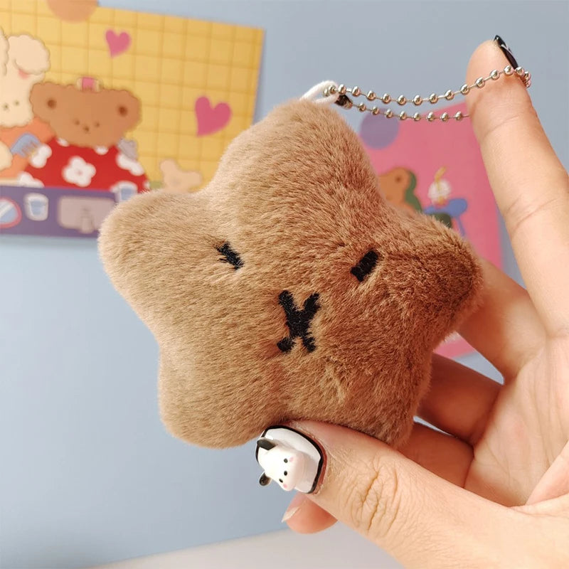 Fuzzy star-shaped kawaii keychain with a face design held by a hand against a colorful background.
