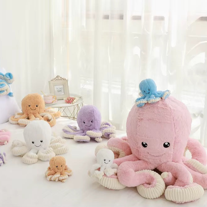 A collection of plush octopus toys in various colors including pink, purple, orange, and white, arranged on a white surface in front of sheer white curtains.
