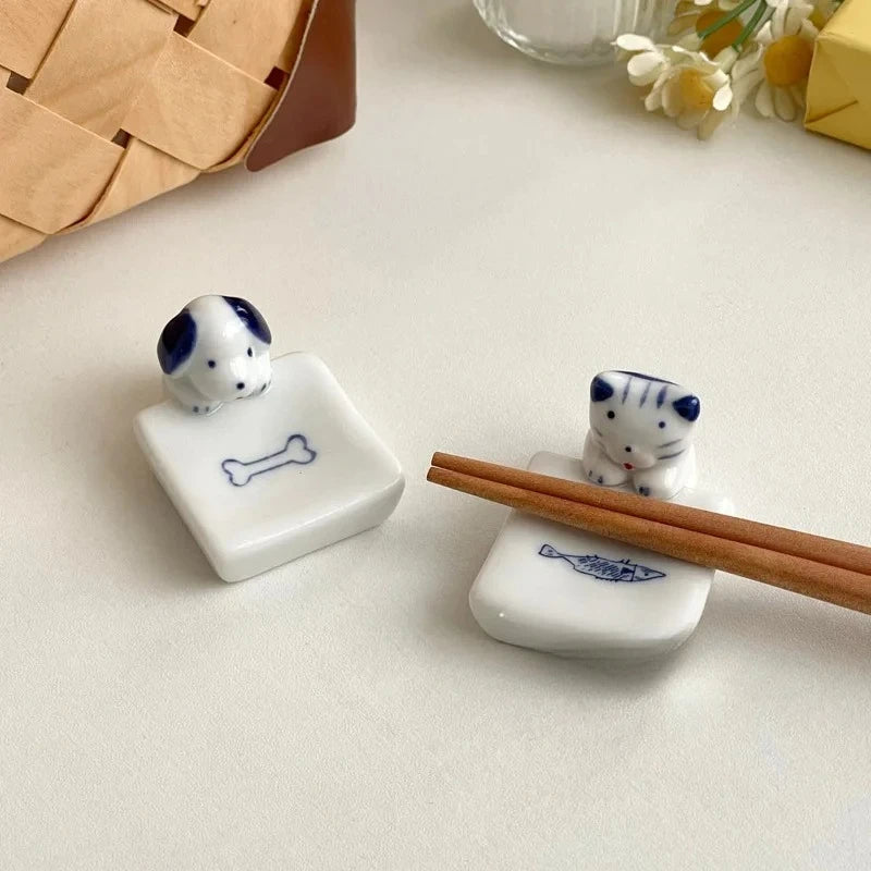 Two ceramic kawaii chopstick holders shaped like dogs with a bone design, one holding chopsticks on a light surface.