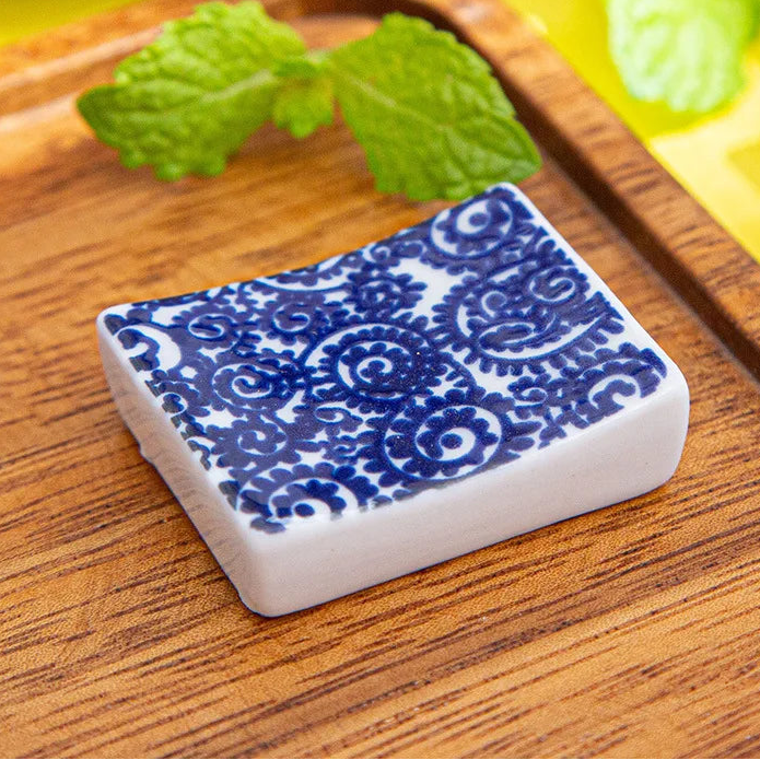 Small rectangular ceramic kawaii chopstick holders with blue and white pattern on a wooden surface with mint leaves.